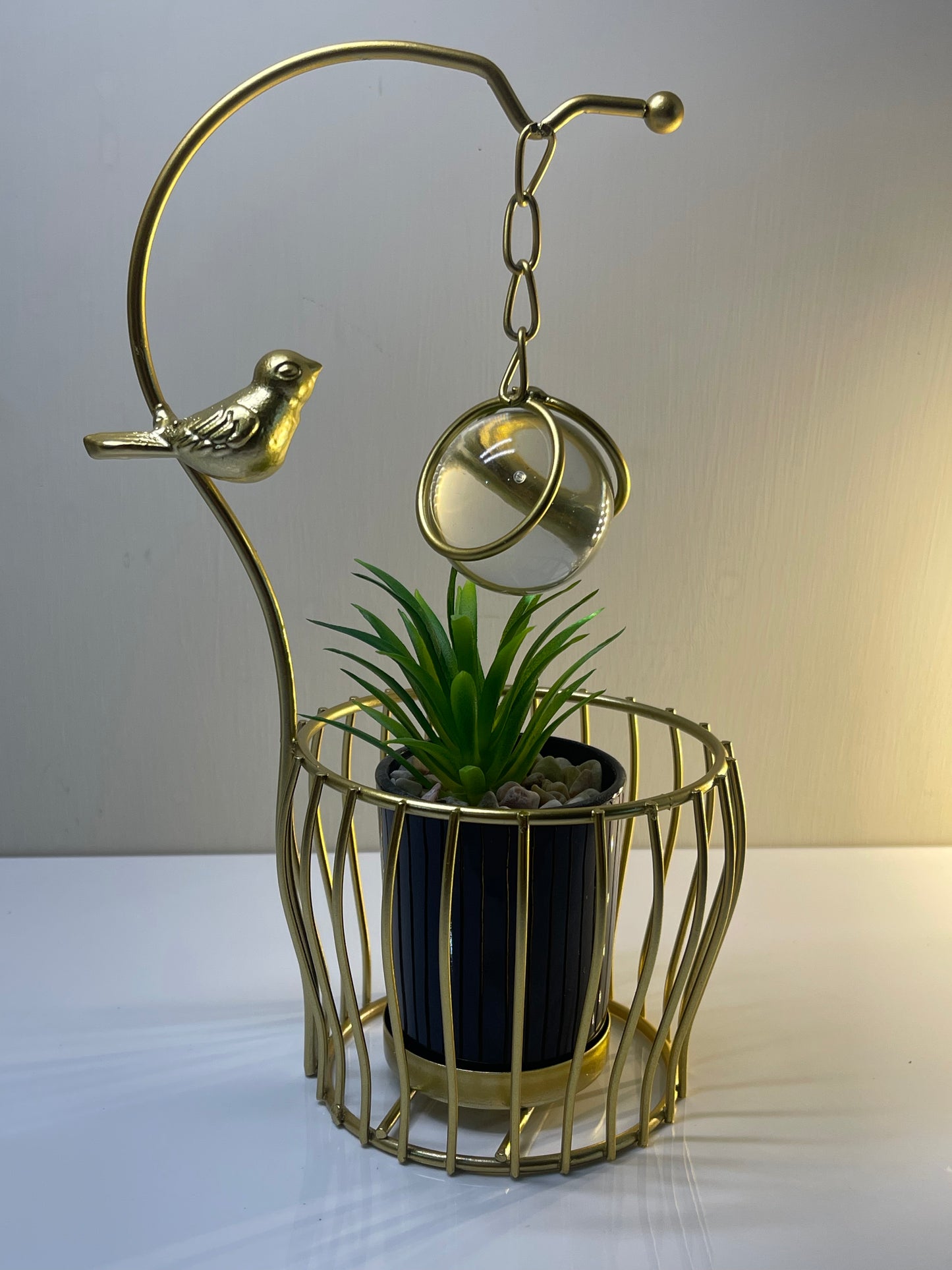 Golden arc planter with a central pot, hanging glass globe, and a bird accent.