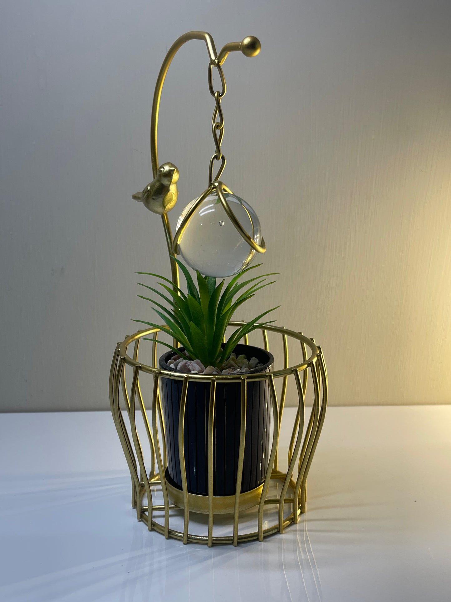 Side view of the golden arc planter featuring a bird and hanging globe.