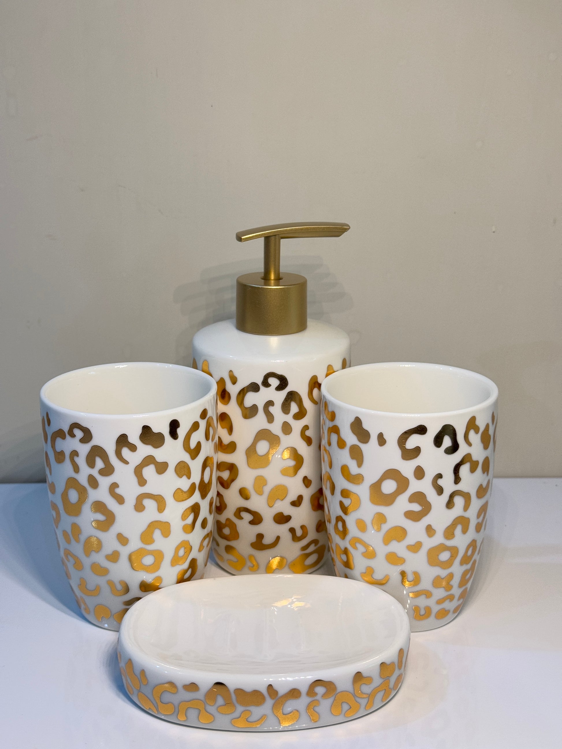 4-piece cheetah print ceramic bathroom set in white and metallic gold, including soap dispenser, tumbler, toothbrush holder, and soap dish.