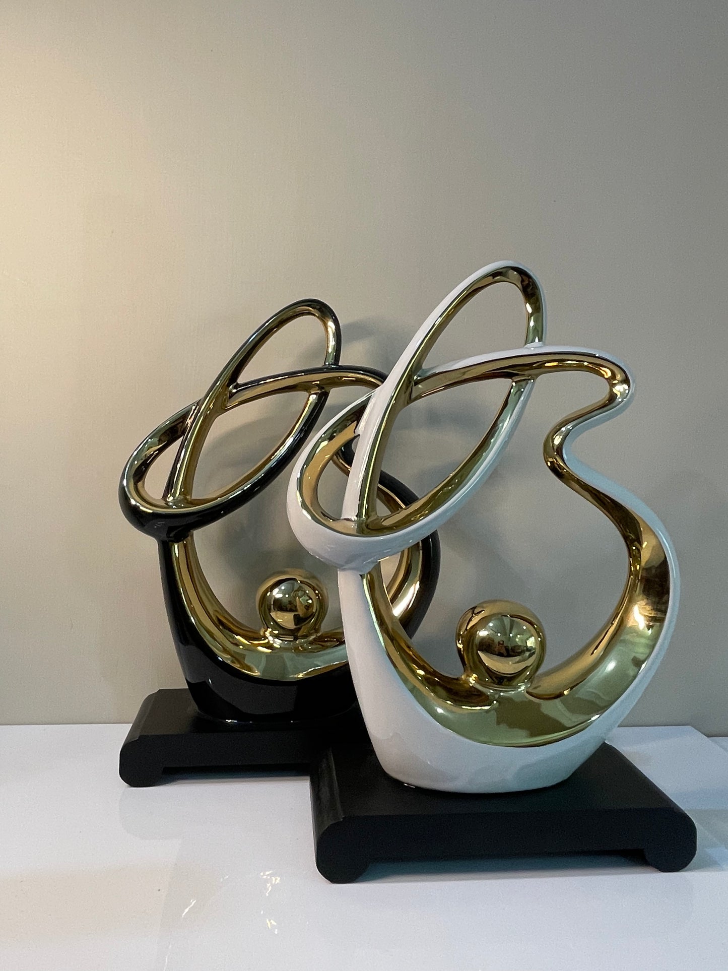 Abstract resin ornament with gold accents, available in black or white, set on a black base.
