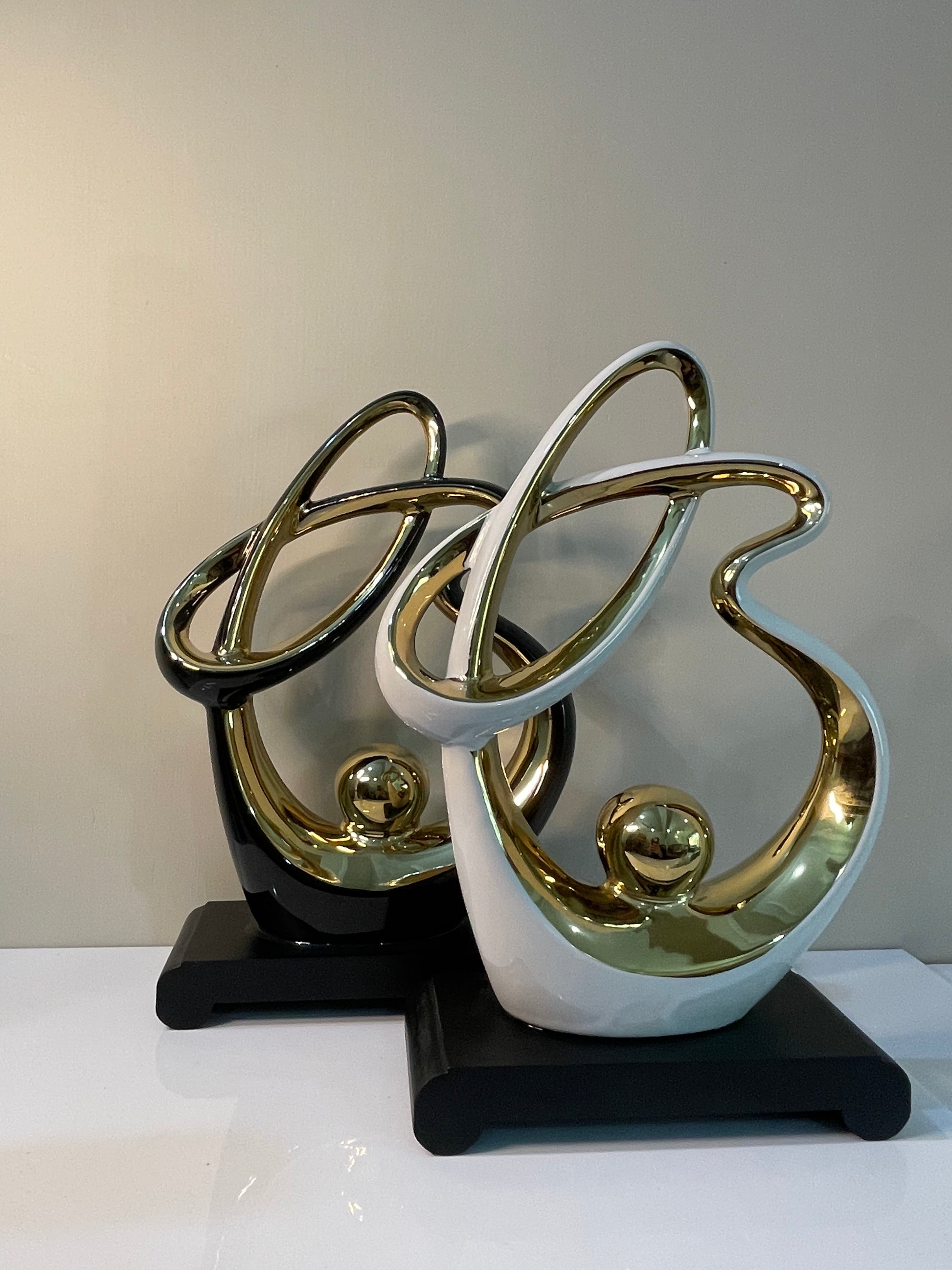 Abstract resin ornament with gold accents, available in black or white, set on a black base.