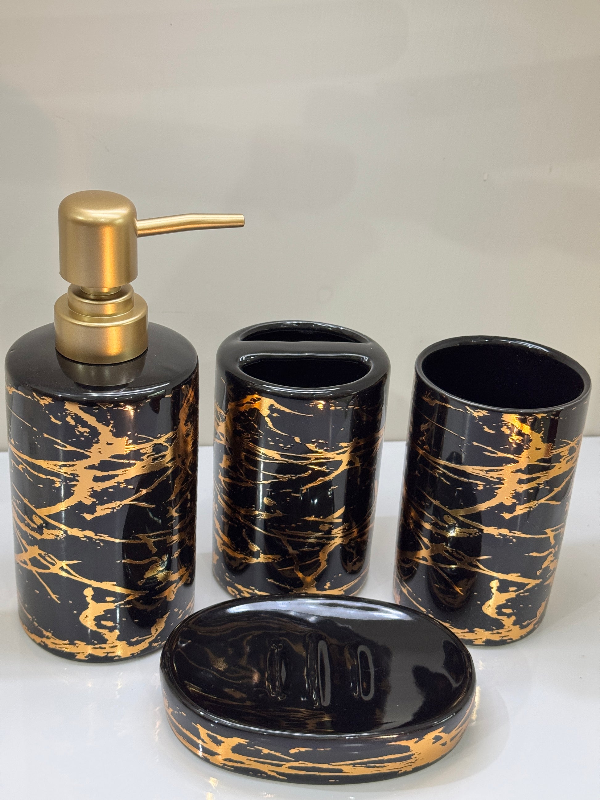 Complete 4-piece ceramic bathroom accessories set in glossy black and gold displayed on a countertop.