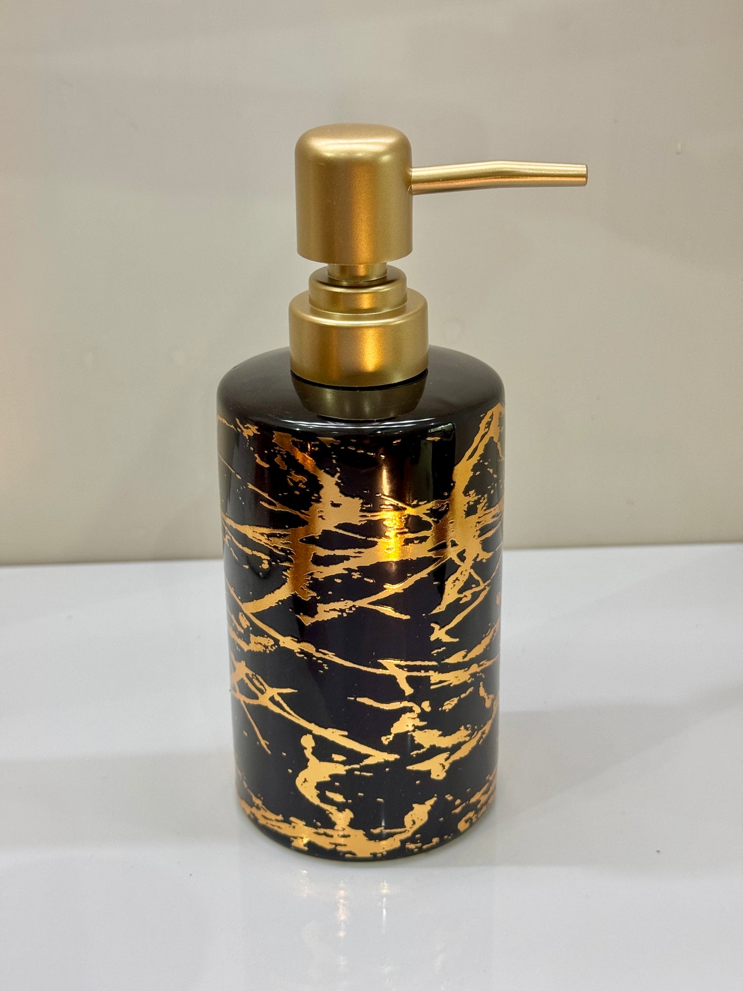 Glossy ceramic soap dispenser with a sleek black and gold design, perfect for modern bathrooms.