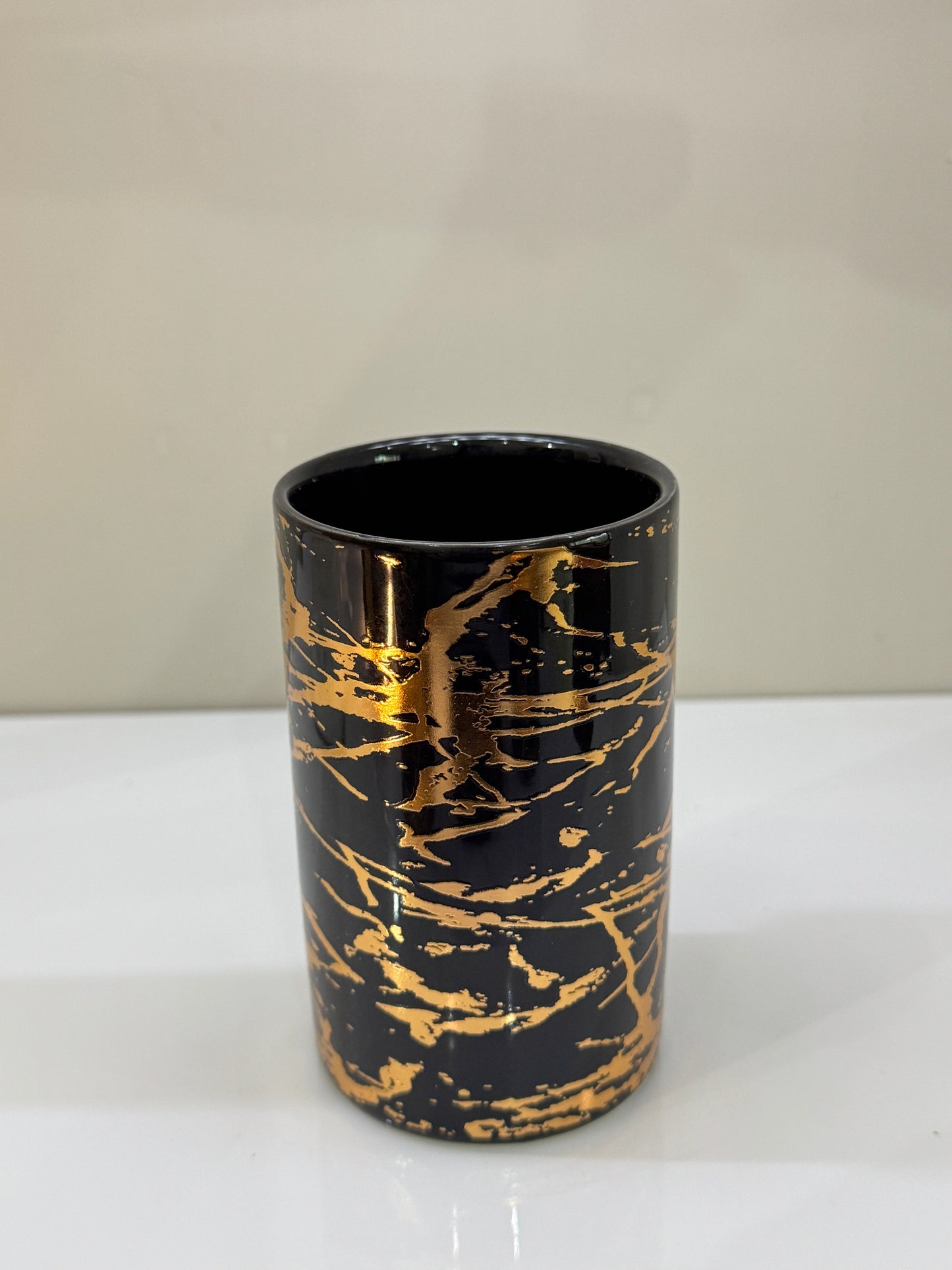 Glossy ceramic tumbler in black and gold tones, ideal for rinsing or holding small bathroom essentials.