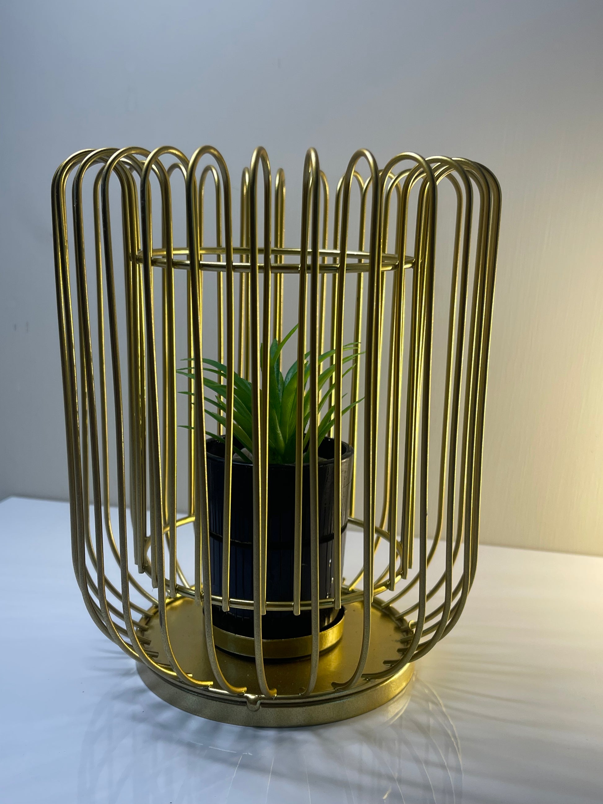 Gold metal cage planter with faux succulent on a tabletop, styled with modern decor.