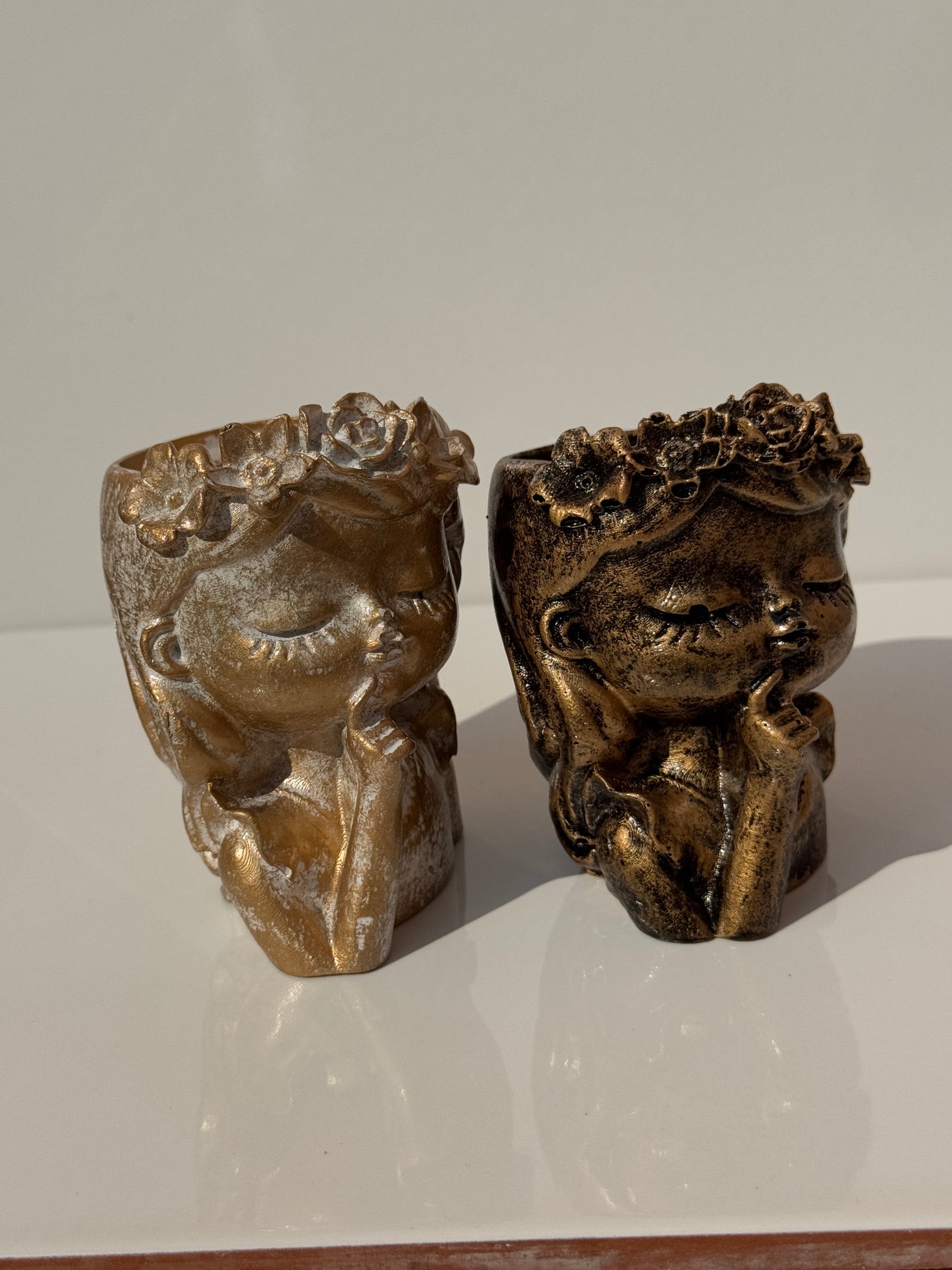 Two Flower Girl Concrete Planters in aged stone, bronze, and plain concrete finishes.